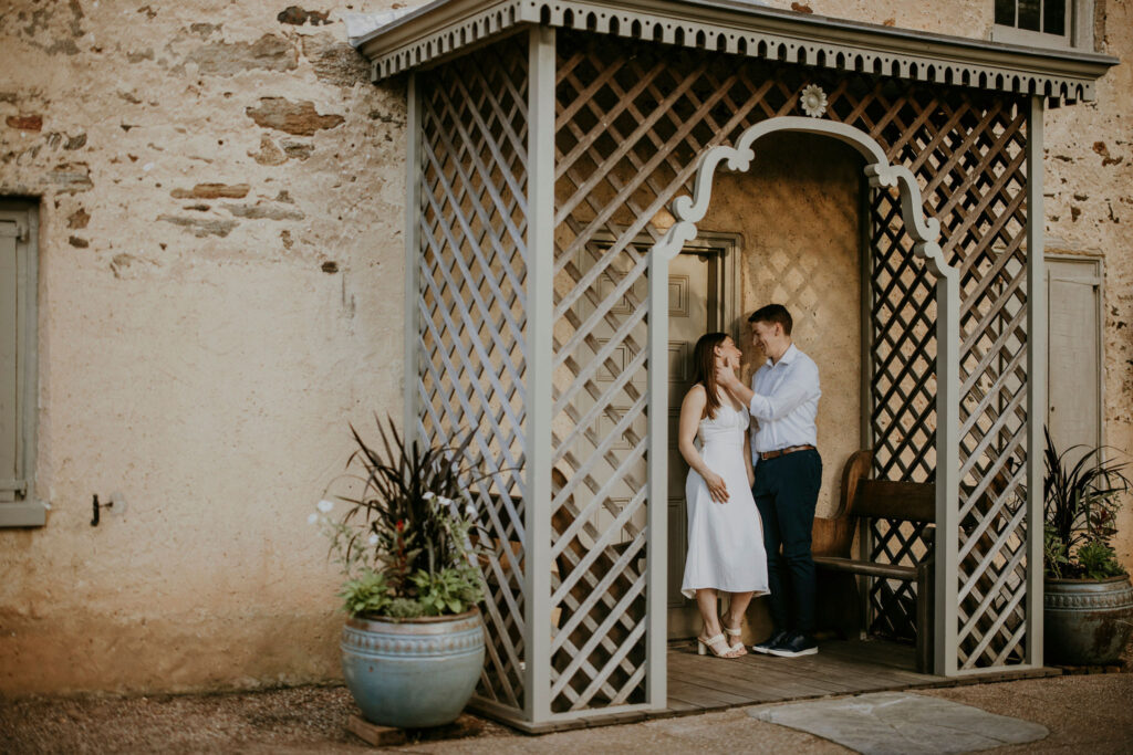 A couple, posed against a wall under a pergola. 