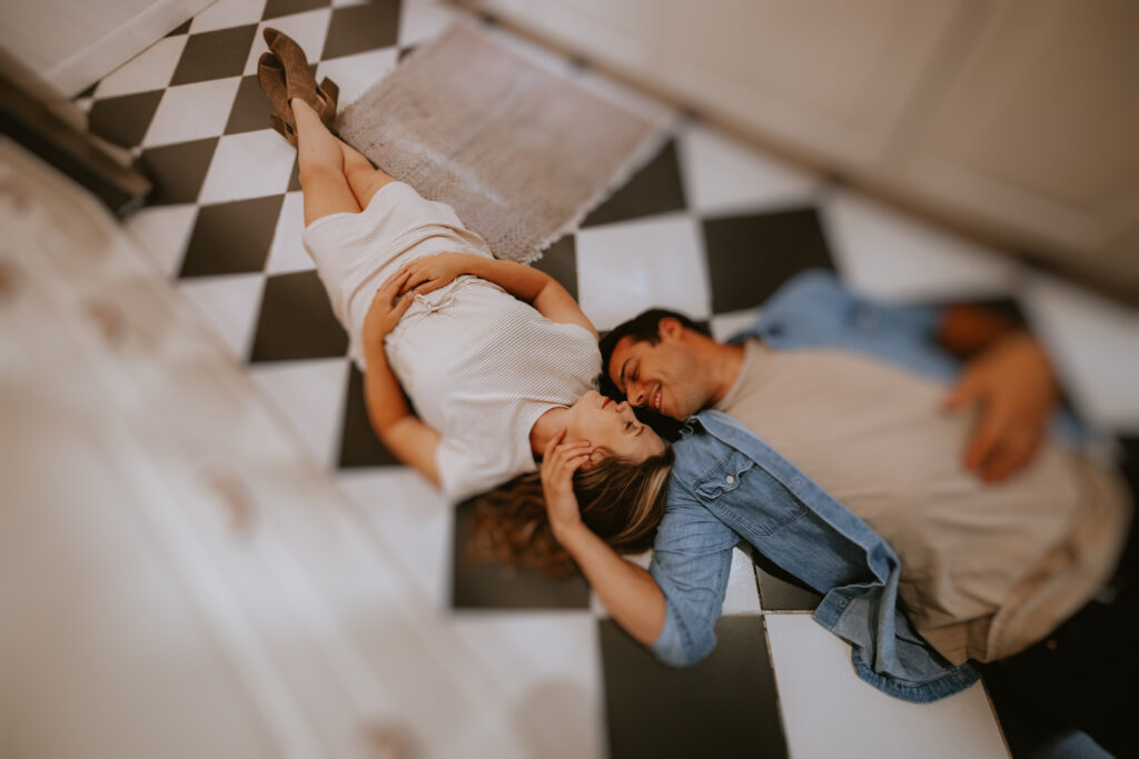 A couple, laying on a black and white checkered floor. 